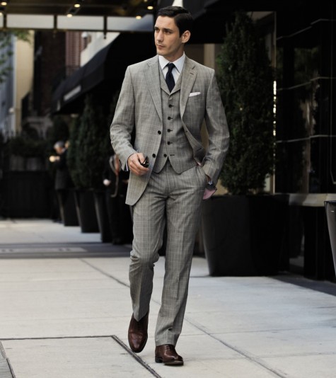 Người đàn ông mặc suit nam ba mảnh kẻ caro xám kèm ghi-lê, cà vạt xanh than và giày da nâu, dạo trên phố